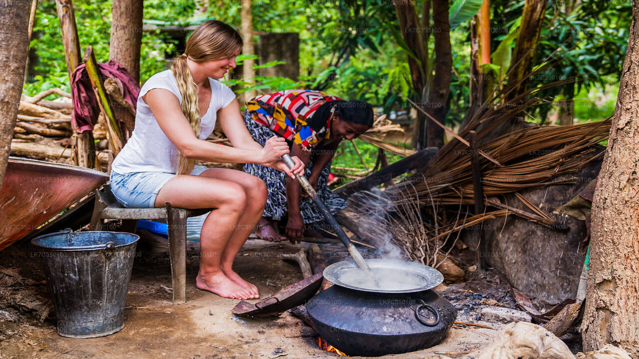 Traditional Sri Lankan village cooking experience with a tourist stirring a boiling pot over an outdoor fire.